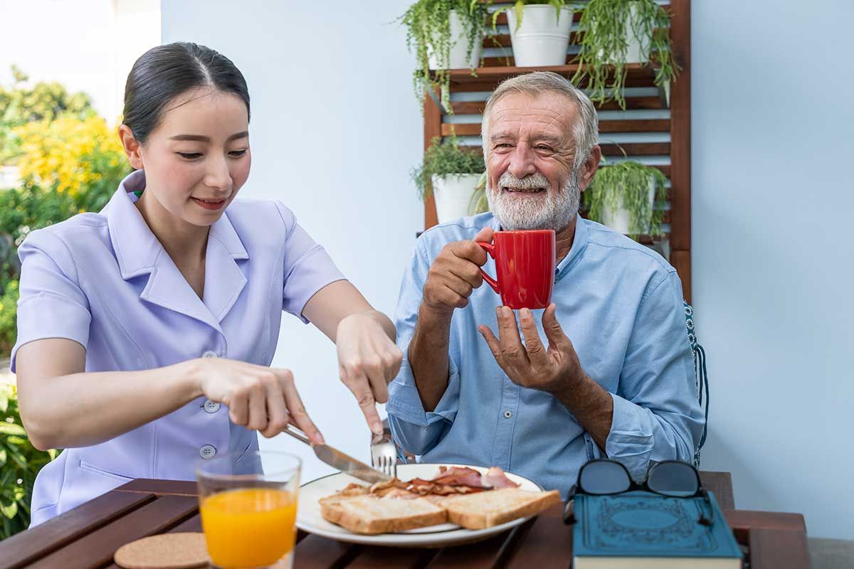 Nurse assist elderly senior man eat breakfast